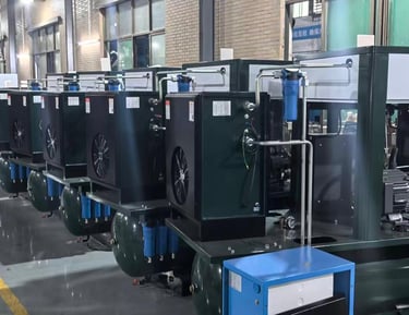 A row of industrial rotary screw air compressors with tanks in a manufacturing facility factory.