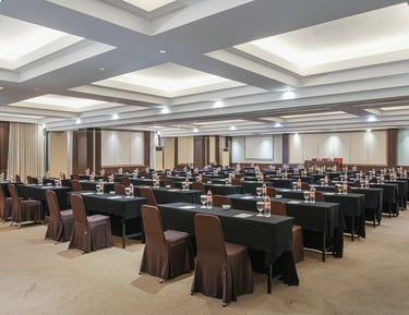 Spacious hotel conference room with rows of tables, brown chairs, and modern recessed lighting.