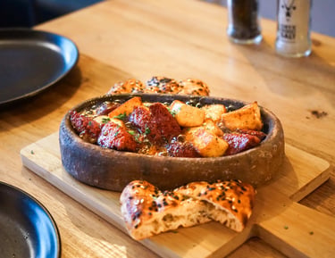Turkish sausage and potato stew served in a stone bowl with flatbread on a wooden board.