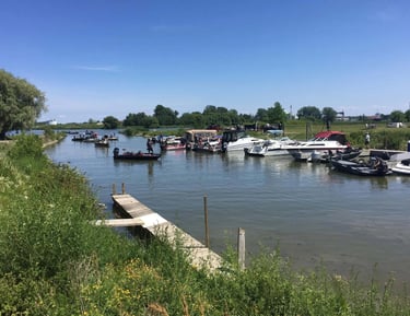 Fishing boats and pleasure crafts docked at a sunny marina along a narrow waterway.