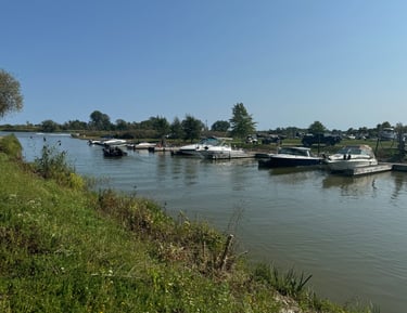 Motorboats and yachts docked along a river marina under a clear blue sky.