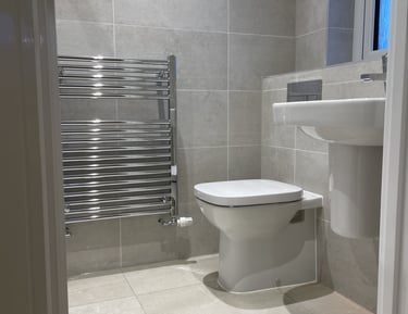 Modern bathroom with grey tiles, a white toilet, pedestal sink, and chrome heated towel rail.