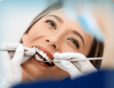 Una mujer joven sonriendo durante un chequeo dental, con un dentista examinando sus dientes 