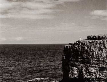 a celebrating figure in the distance, at the top of a peak surrounded by water