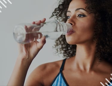 A curly-haired woman in fitness apparel drinking fresh water from a bottle to stay hydrated.