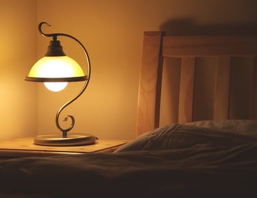 Vintage wrought iron bedside lamp with warm glow on a wooden nightstand next to a bed.