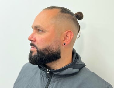 Side profile of a man with a skin fade, full beard, and tied top knot — clean finish and modern style from Yau Barber Studio.