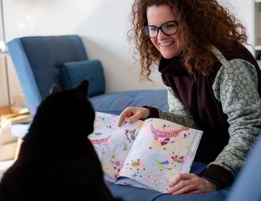 Une illustratrice qui montre son livre jeunesse à son chat noir