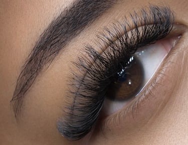 Close-up of a brown eye with long, voluminous volume eyelash extensions and a shaped eyebrow.