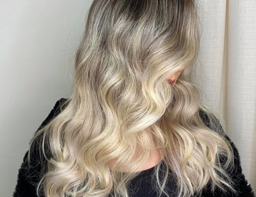 A woman with wavy ash blonde balayage hair featuring dark roots and beach waves.