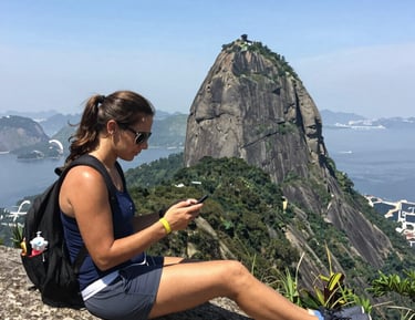 Two women chatting happily while using their phones outdoors in a sunny Brazilian park.