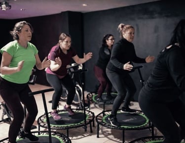 Un grupo de mujeres participando en una clase de salto en trampolín de alta energía en un gimnasio.