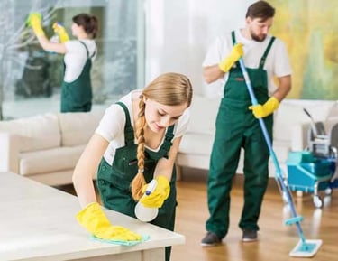 Professional cleaning crew in green overalls sanitizing a modern office using microfiber cloths and mops.