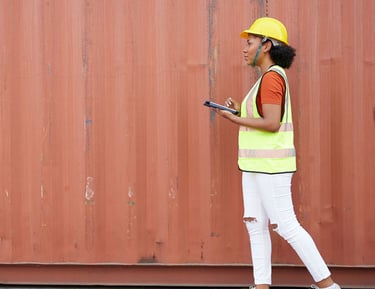 Female logistics manager in hard hat using a digital tablet by a red shipping container.