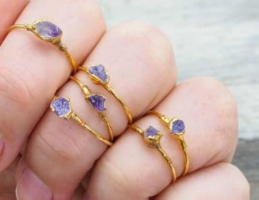 Mano con cinco delicados anillos de oro, cada uno con cristales de amatista púrpura