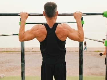 Muscular man performing pull-ups at an outdoor calisthenics gym on the beach.