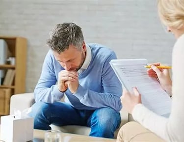 Femme aidante écoute un homme penché en avant coudes sur ses cuisses