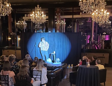 a man standing on a stage with a spotlight shining on him while he holds a microphone