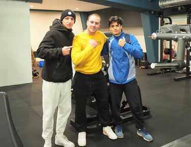 Tre giovani atleti sorridenti posano insieme nella palestra Move 2 Grow a Milano, circondati da attrezzature per l'allenament