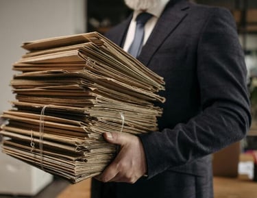 Un hombre de negocios con traje lleva una gran pila de archivos en papel y documentos en una oficina