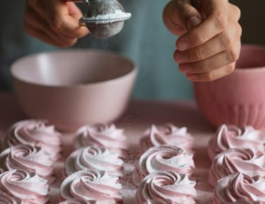Un panadero espolvoreando panqueques en espiral rosa con azúcar glas usando un colador.