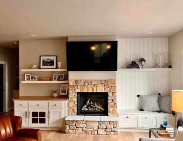 Modern farmhouse living room featuring a stone fireplace, wall-mounted TV, and white built-in shelving.