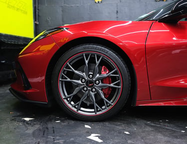 Red Chevrolet Corvette C8 featuring custom alloy wheels and red brake calipers in a professional garage.