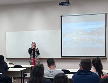 Female professor leading a university lecture in a classroom with students and a projector screen.