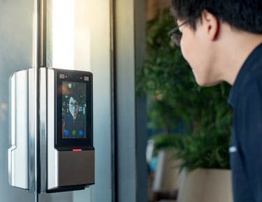 A person using a facial recognition access control system on a glass door for biometric security.