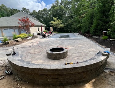 Custom stone paver patio installation featuring a built-in fire pit and curved retaining wall.