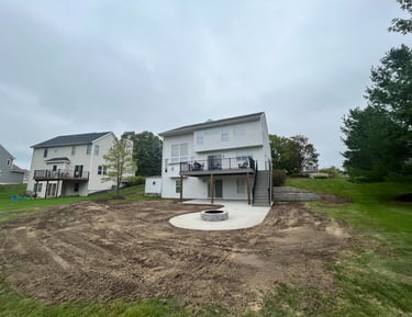 Two-story white house featuring a new backyard adding concrete patio with a stone fire pit.