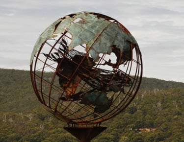 Verdigris metal globe sculpture on the beach with a mother whale and her calf in the middle of it