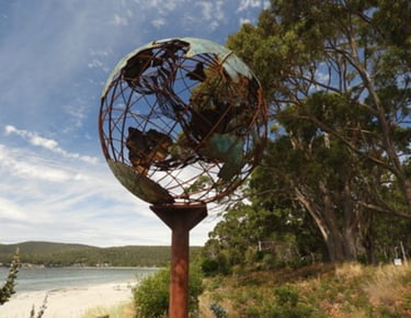 Verdigris metal globe sculpture on the beach with a mother whale and her calf in the middle of it