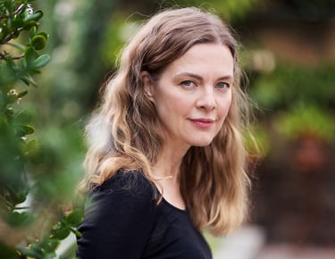A beautiful middle-aged woman with long curly hair and a black shirt standing in a garden and looking at the camera