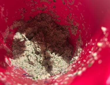 Freshly blended green herb and garlic paste inside a red mixing bowl for cooking.