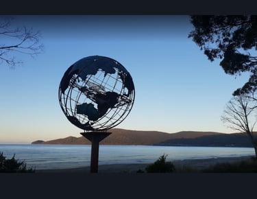 Verdigris metal globe sculpture on the beach with a mother whale and her calf in the middle of it
