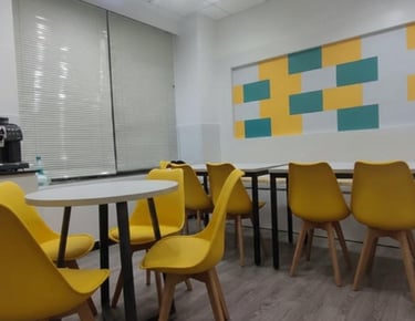 Modern office breakroom with vibrant yellow chairs, round tables, and a coffee machine.
