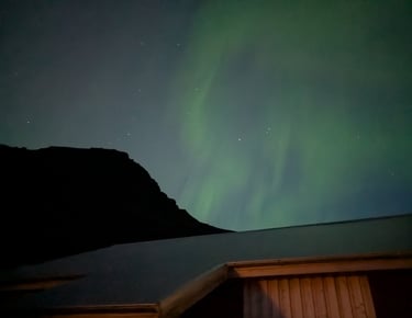 Green aurora borealis glowing in a starry night sky above a dark mountain in Iceland.