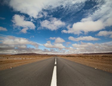 A Moroccan desert road with painted white lines receding into the distance