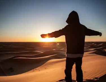 Man standing on a Sahara dune at sunset with arms outstretched during Ultimate Sahara trek