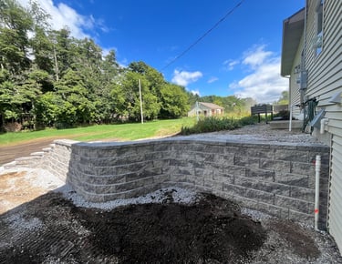 Newly installed grey stone retaining wall in a residential backyard with landscaping and green lawn.