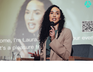a woman in a suit and a microphone in front of a screen while ohaio livespeaker works