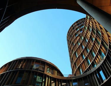 Vista inferior de edifícios contemporâneos com formas curvas, estruturas metálicas e céu azul.