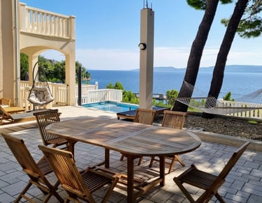 The photo shows a dining table, deck chairs and swings in the central courtyard overlooking the pool and the open sea.