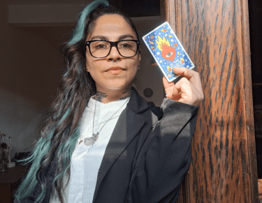 Mujer con lentes sosteniendo una carta de tarot con un corazón en llamas