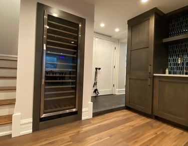 Modern home bar featuring a built-in wine cooler, dark cabinetry, and hardwood floors near a staircase.