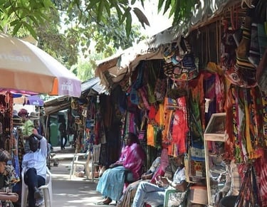 Local vendors at an outdoor African craft market selling colorful handmade textiles and bags.