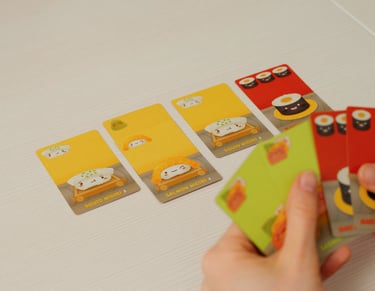 Rankoje laikomos ir ant stalo padėtos Sushi Go žaidimo kortos