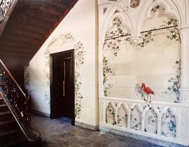 Hallway with wooden staircase and large mural of faux sandstone, ivy, gothic arches, and red bird.