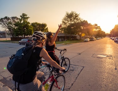 Image of two women bikers riding in the street, one with her arm stretched up in celebration